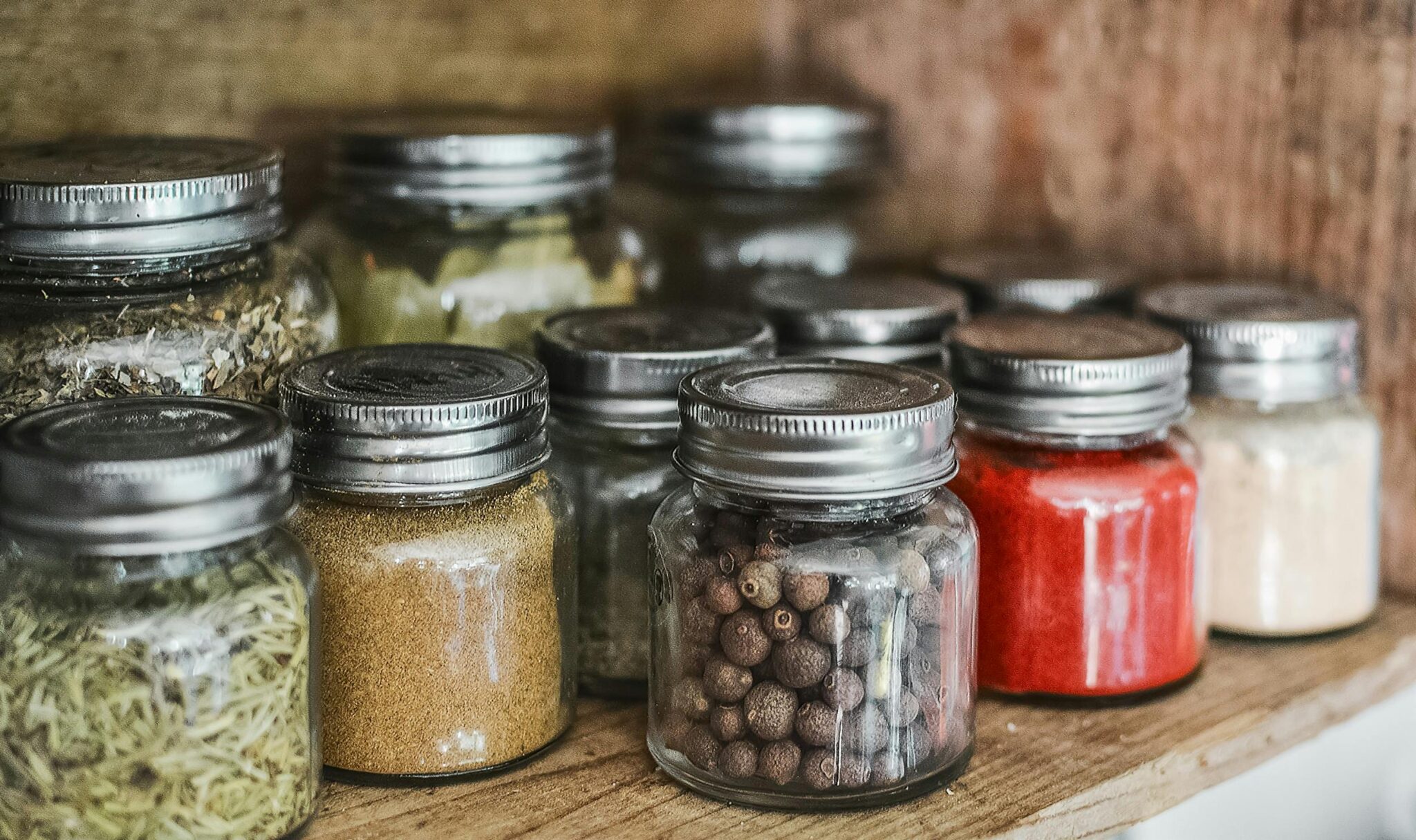 Close-up of assorted spice jars with various herbs on a kitchen shelf, showcasing colorful culinary ingredients.